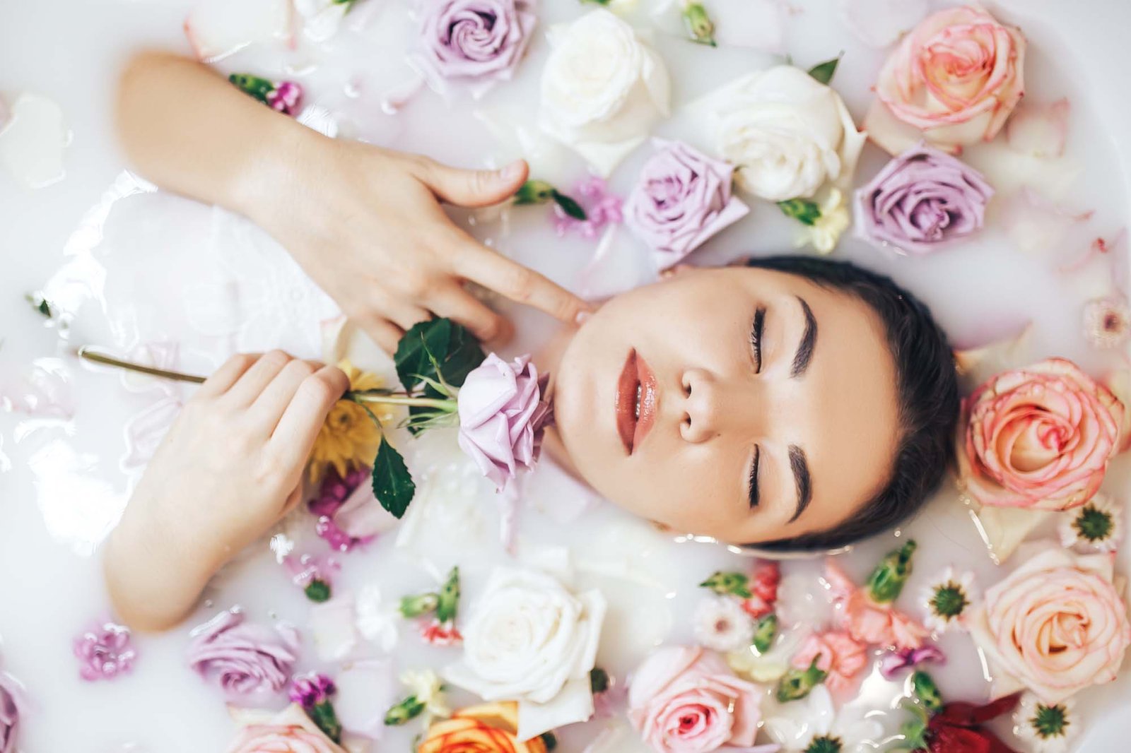 The woman takes a wellness bath filled with milk. The buds of multi-colored roses float on the surface. Relaxing and anti-aging treatments..